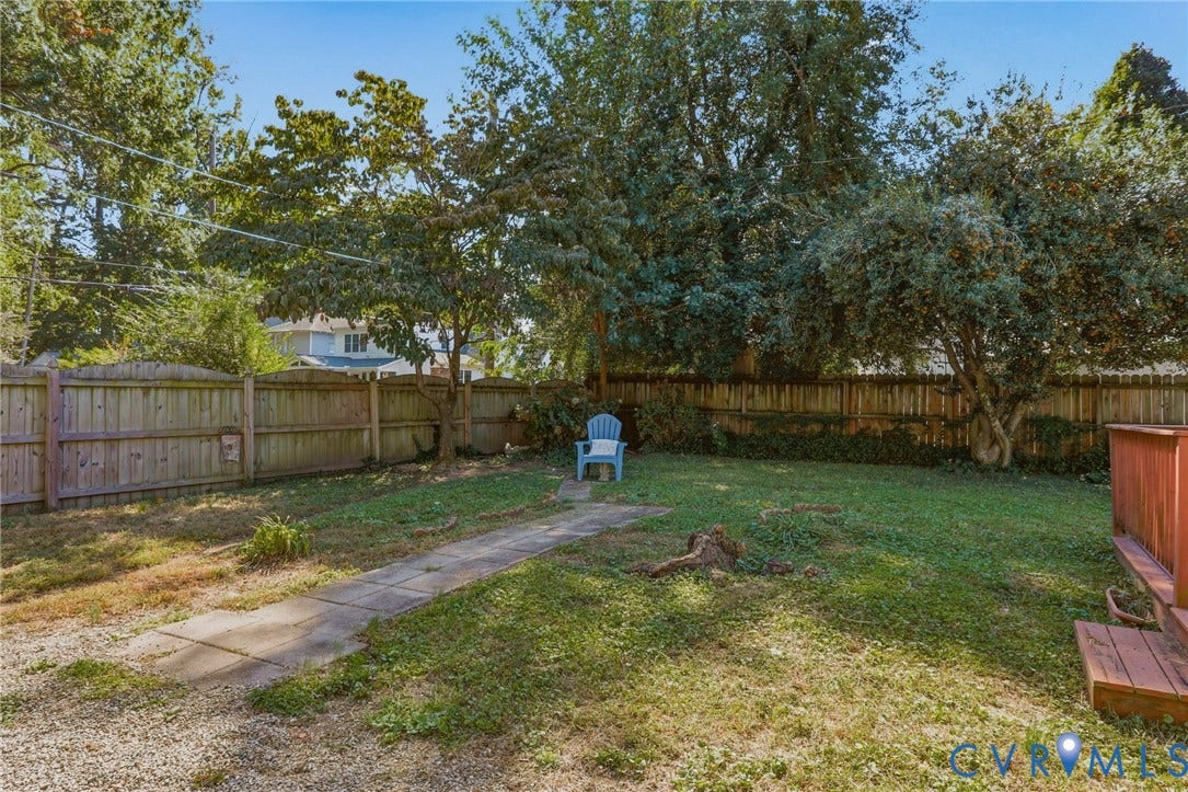 Fenced backyard featuring mature trees, a wooden deck, and a concrete paver pathway