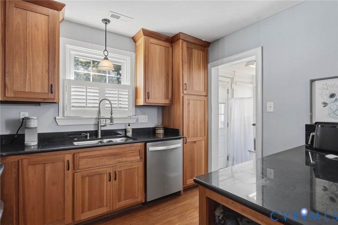 Wood cabinetry, dark countertops, stainless steel dishwasher, undermount sink with gooseneck faucet, and wood-finish flooring