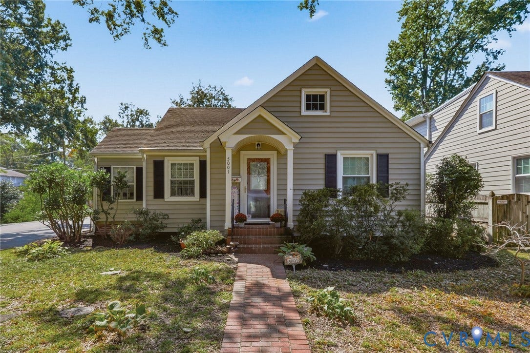 Gable roof home featuring light-colored siding, dark shutters, and a brick pathway