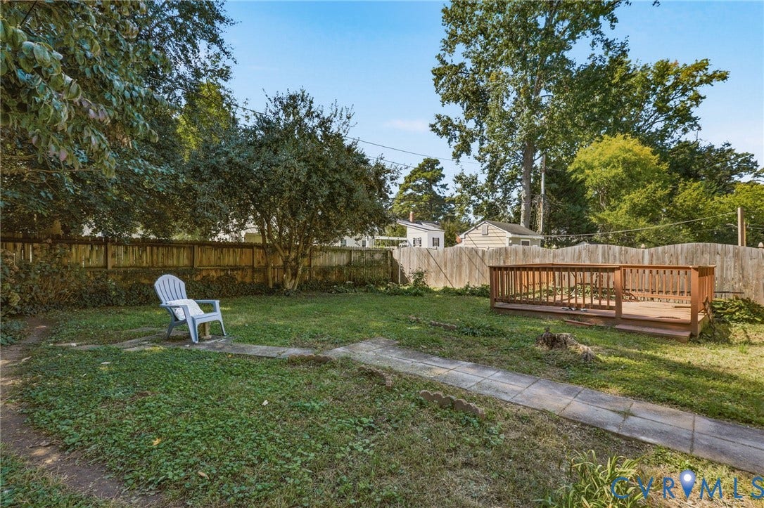 Expansive backyard featuring a wood privacy fence, mature trees, a ground-level wood deck, and a concrete pathway
