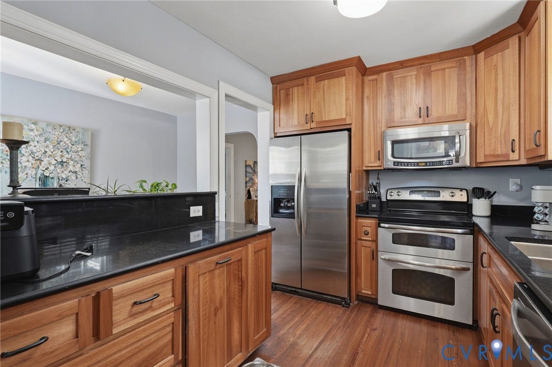 Wood-finish flooring, stainless steel appliances, black countertops, wood cabinetry, and a pass-through window