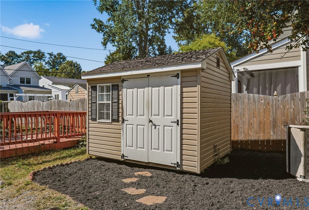 Detached storage shed with shingle roofing, double panel doors, and a window with shutters