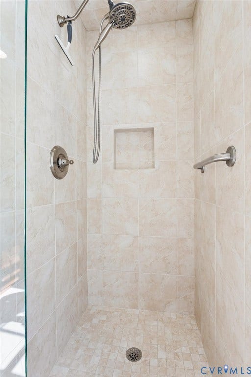 Tiled shower with a niche, handheld showerhead, grab bar, and glass enclosure