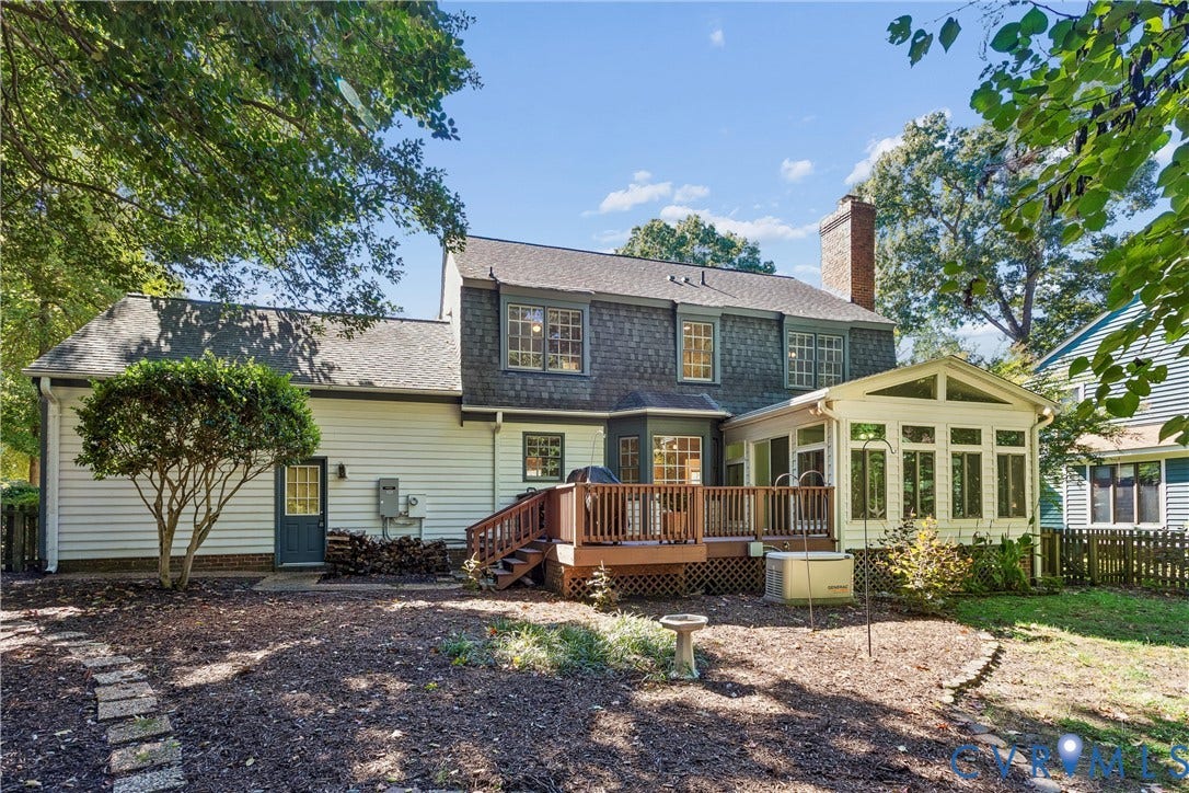 Rear exterior featuring a multi-level wood deck, a sunroom with expansive windows, a brick chimney, and a stone walkway