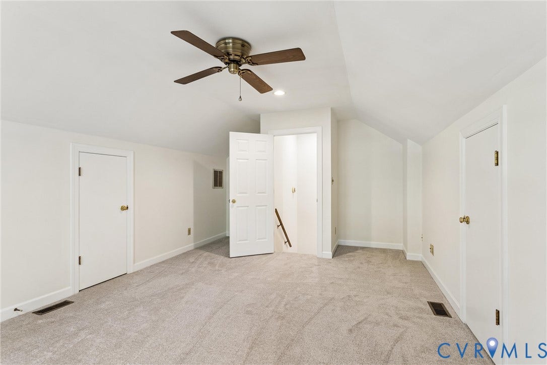 Light gray carpeted flooring, white walls, and a ceiling fan with brass accents