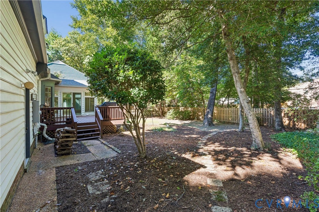Multi-level wood deck, expansive natural backyard, mature trees, privacy fencing, and stone pathway