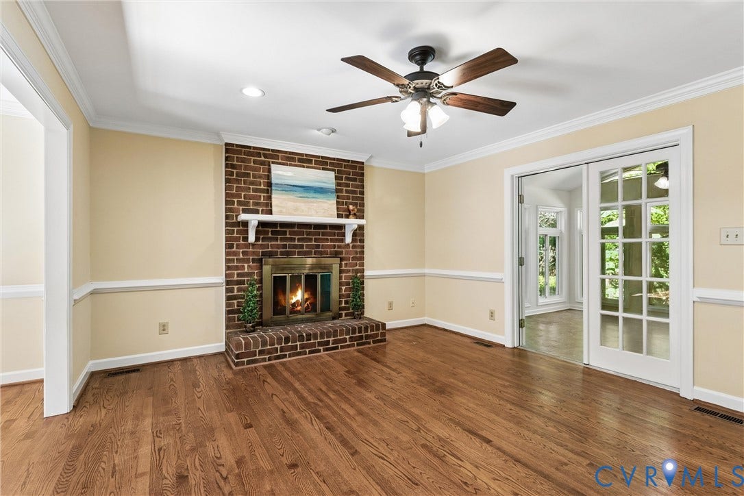 Brick fireplace with a brass firebox, hardwood flooring, ceiling fan, crown molding, and French doors