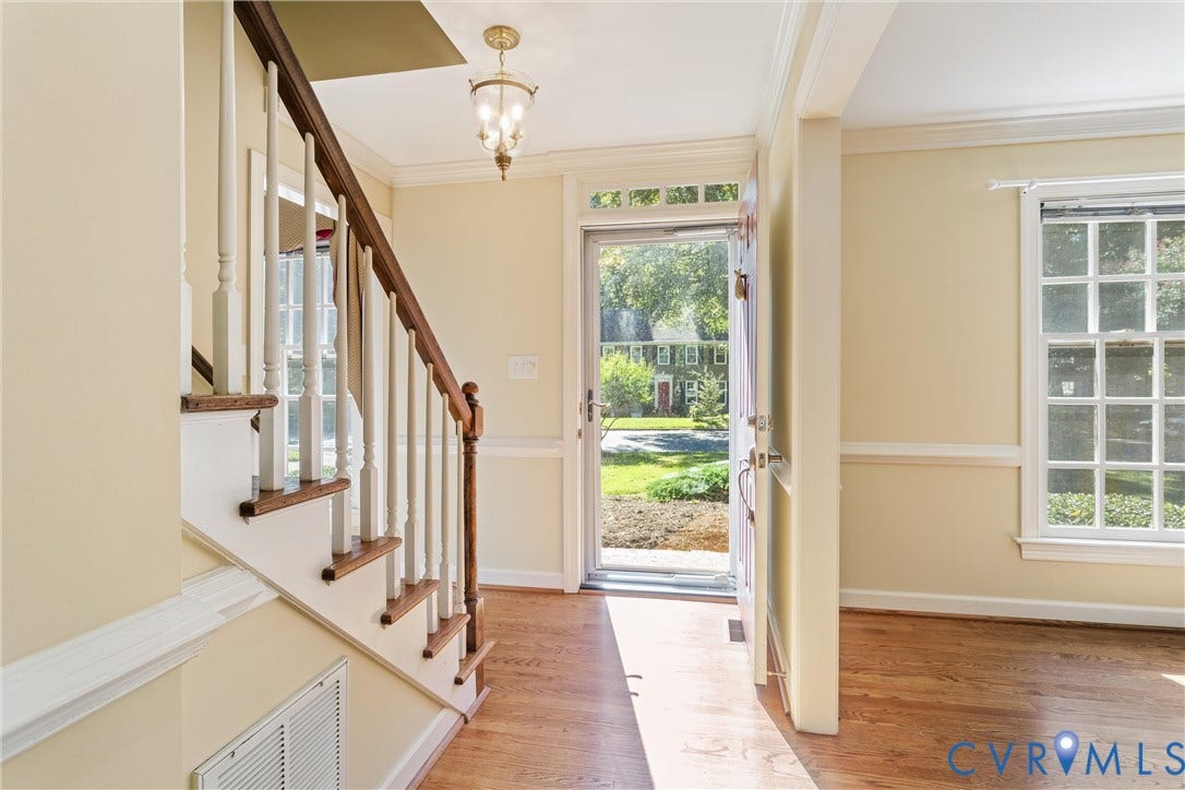 Wood-finish flooring, staircase with wood handrail and white spindles, traditional chandelier, multi-pane window, and transom window above the entry door
