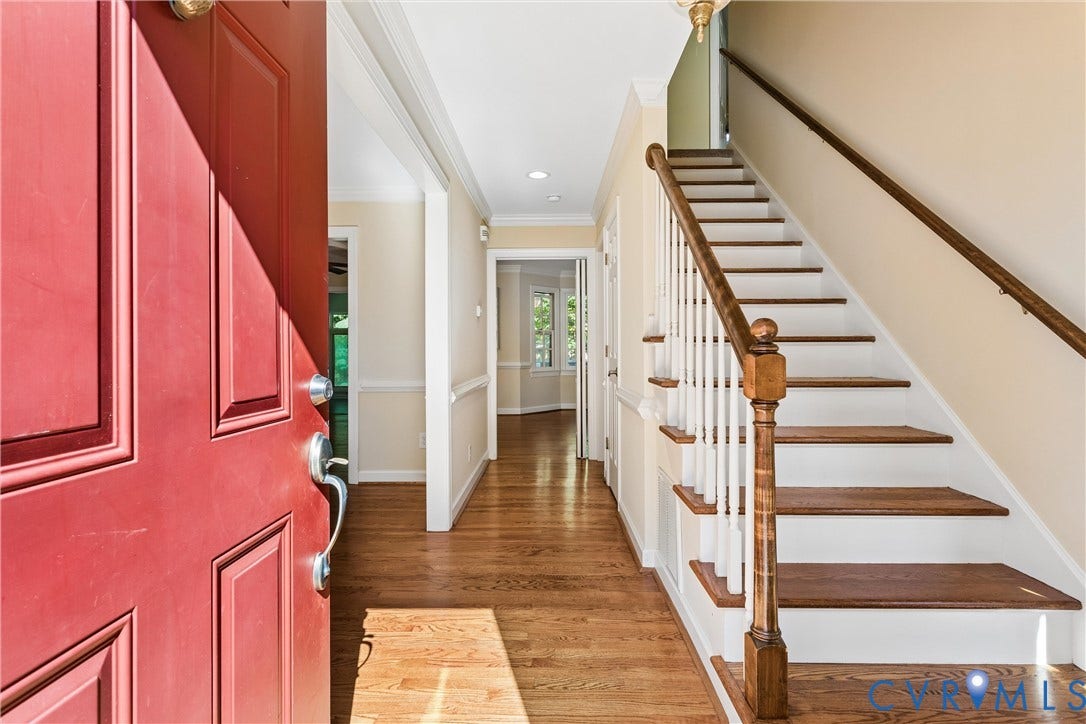 Red paneled entry door, hardwood flooring, white crown molding, white chair rail, and a wooden staircase with white risers and balusters