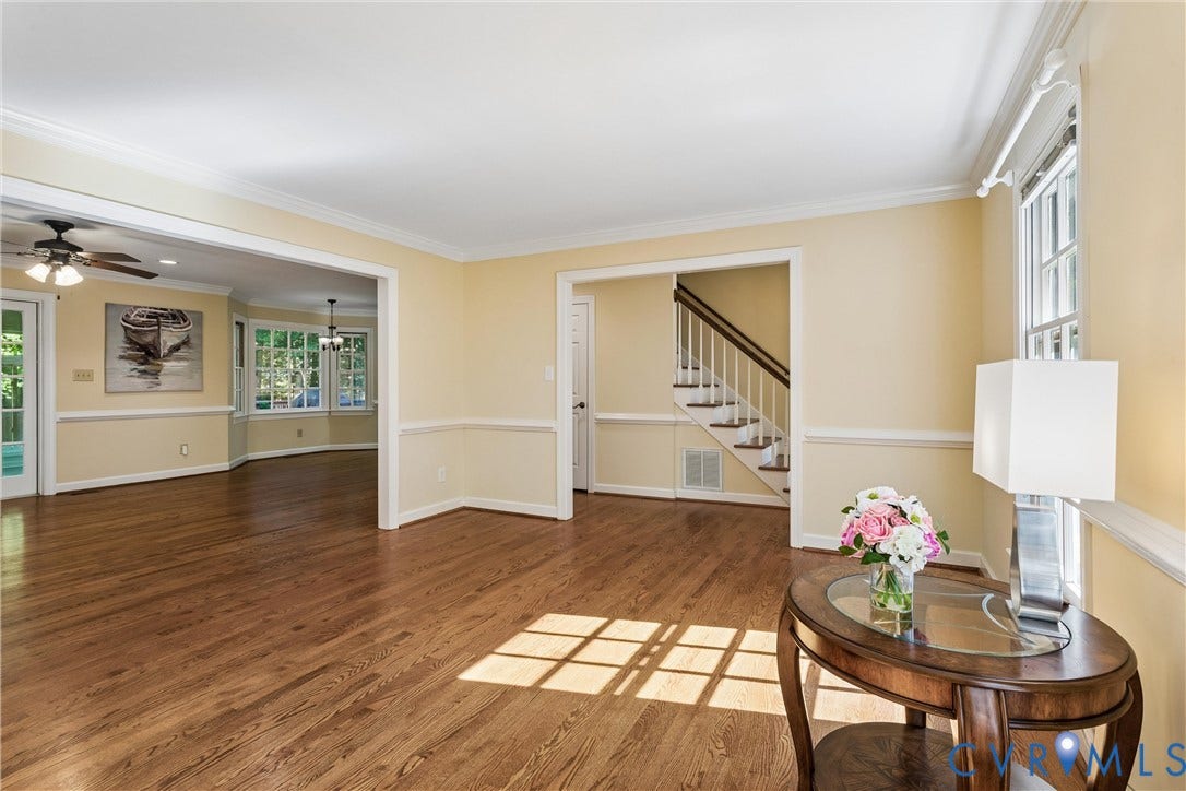 Hardwood flooring, crown molding, chair rail detailing, white trim, and a staircase with white risers and dark wood handrails