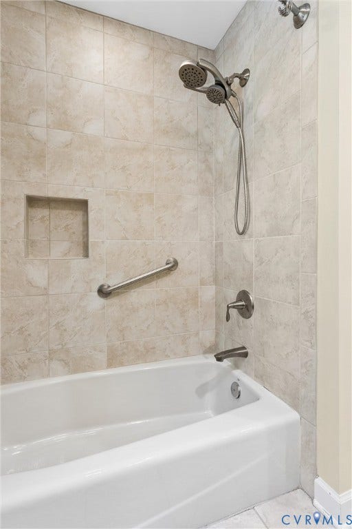 Bathtub with tiled surround, brushed nickel fixtures, shower niche, and grab bar