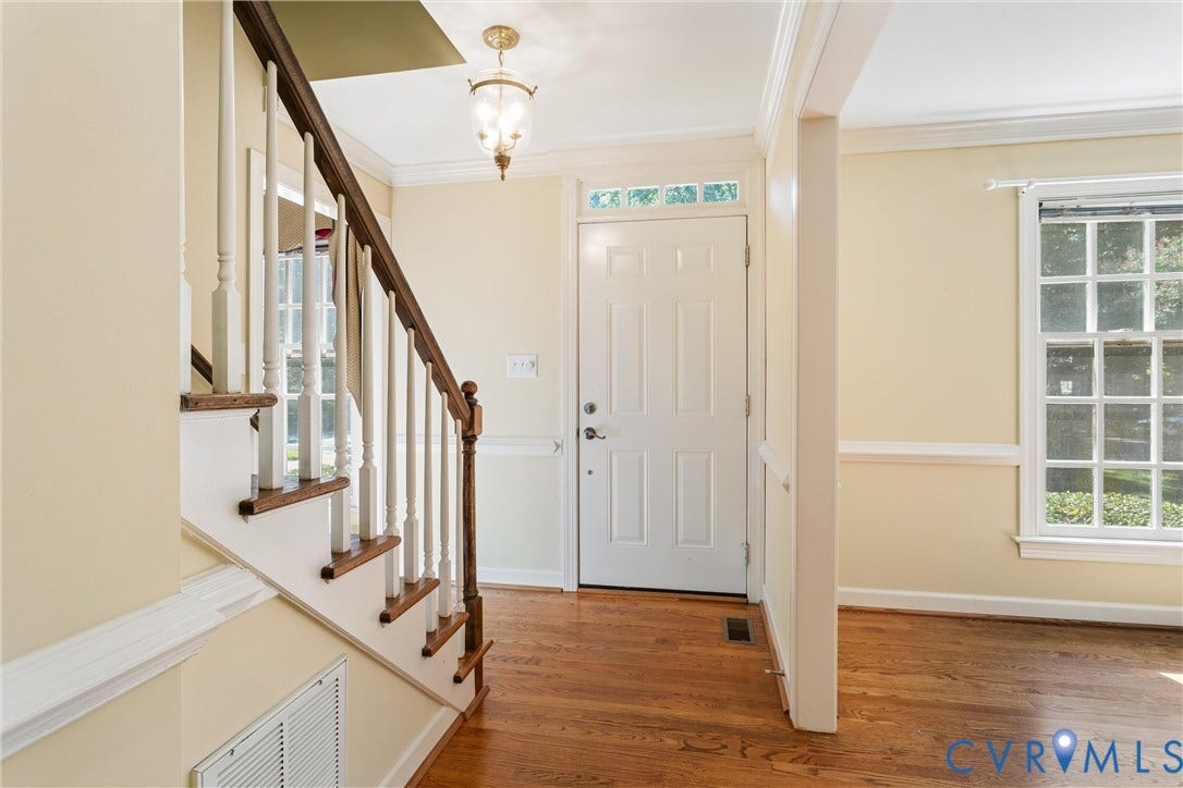 Hardwood flooring, paneled front door with transom window, traditional staircase with wood treads and balusters, and crown molding