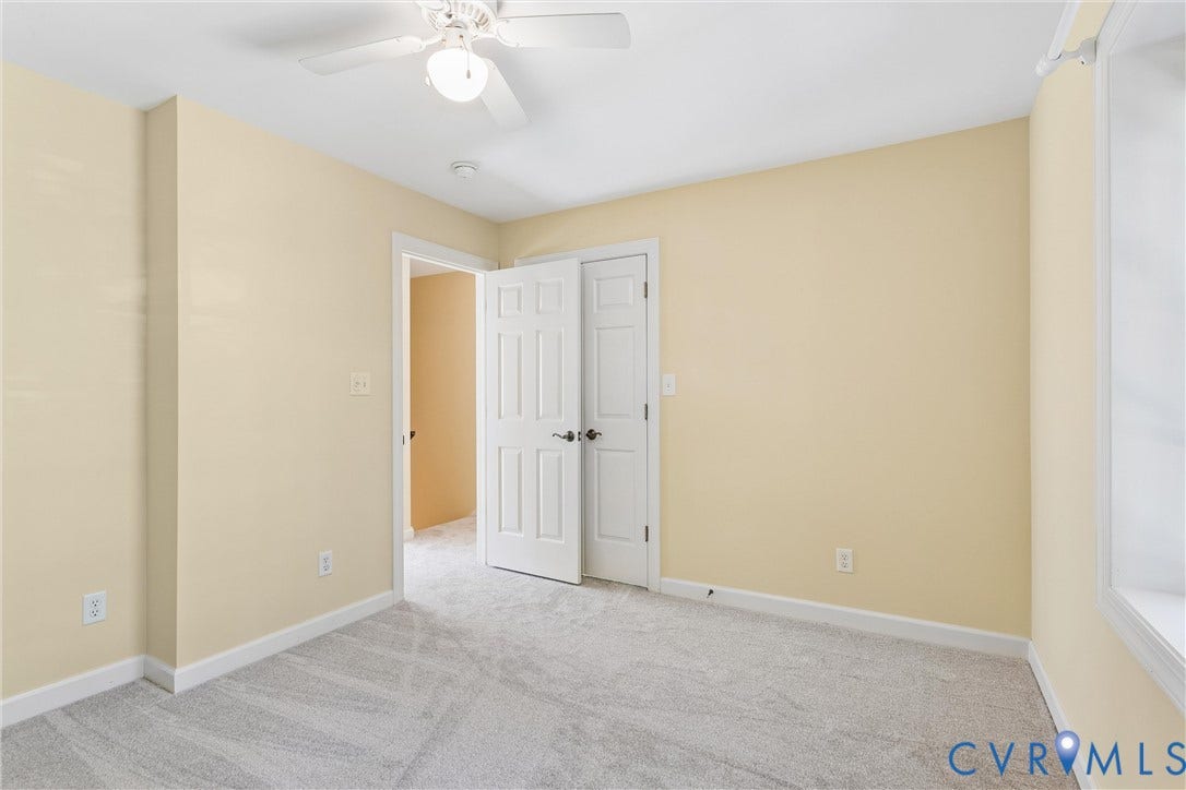 Neutral-toned wall paint, light gray carpet, white trim, white ceiling fan with integrated lighting, and white paneled doors