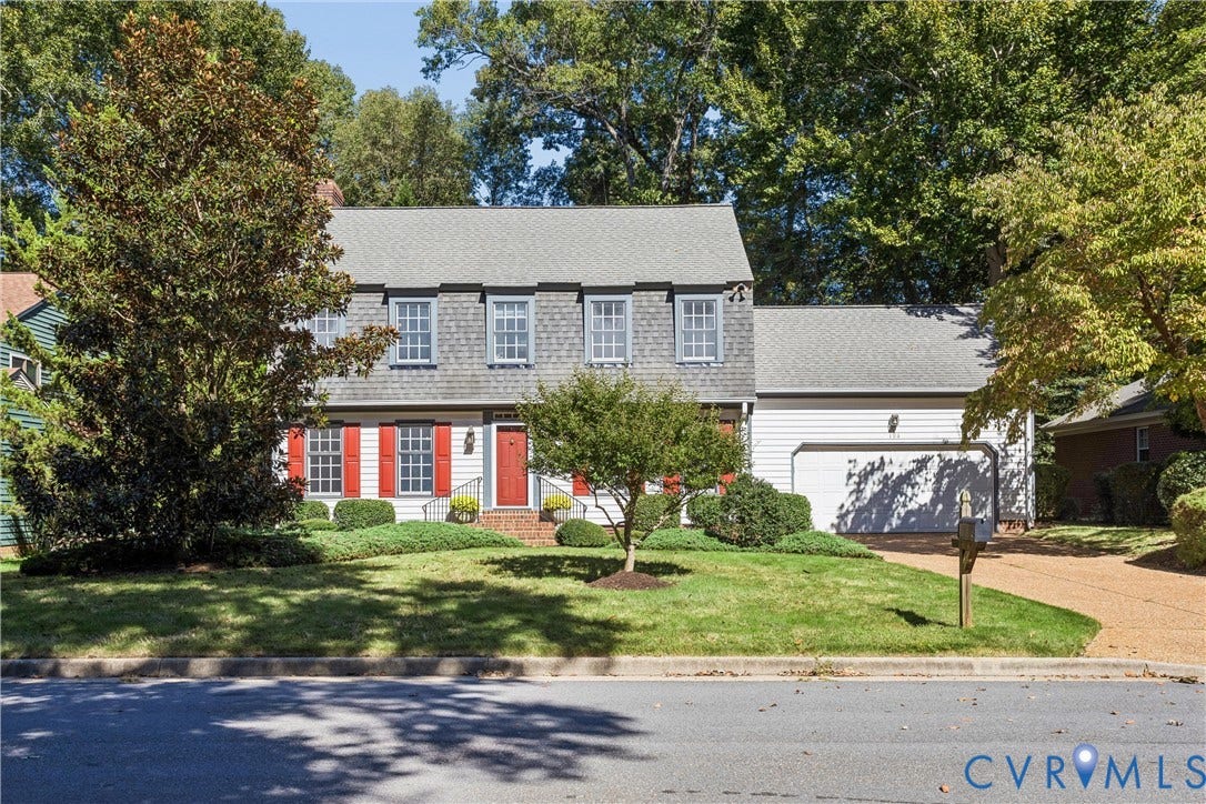 Colonial-style residence featuring a prominent red entry door, red window shutters, and a shingle-sided upper level