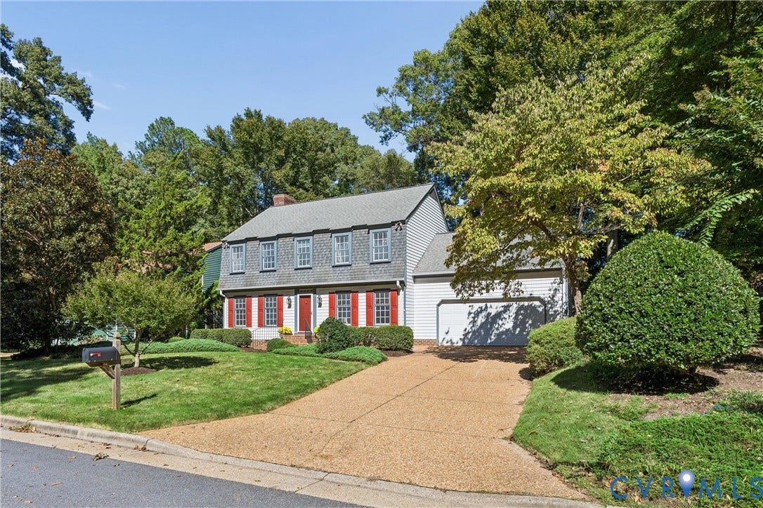 Traditional-style residence with red shutters, a two-car garage, and a gravel driveway