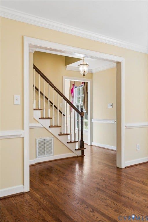 Hardwood flooring throughout the entry, staircase with painted risers and dark wood handrail, crown molding, and wainscoting