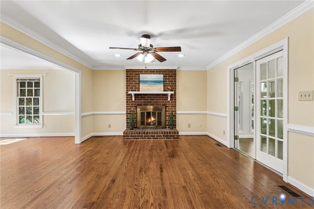Spacious living room featuring gleaming wood-finish flooring, cream-colored walls with chair rail detailing, and a brick fireplace with gas insert