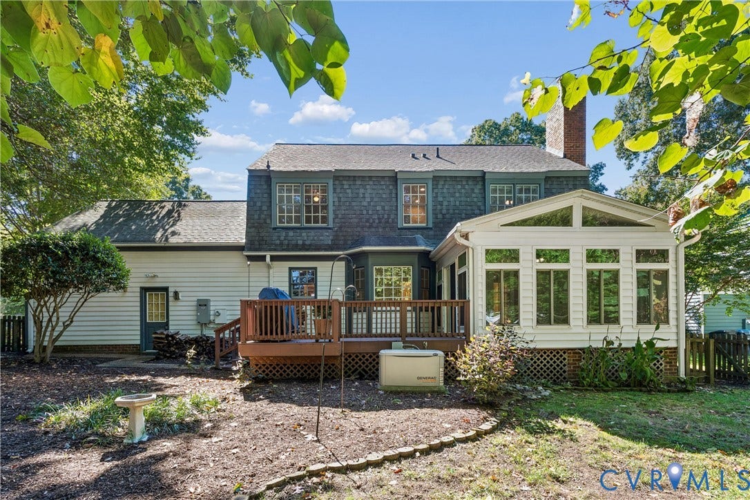 Two-story exterior with a wood deck, a sunroom with large windows, and a brick chimney