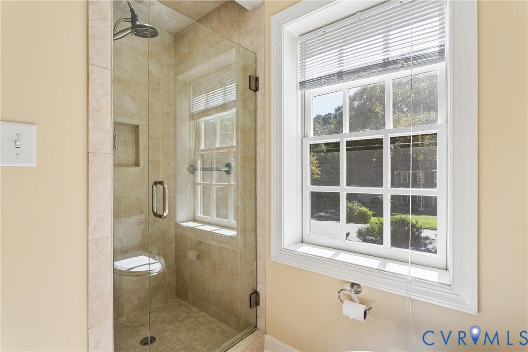 Glass-enclosed shower with tiled walls and flooring, featuring a built-in shower niche and a showerhead fixture