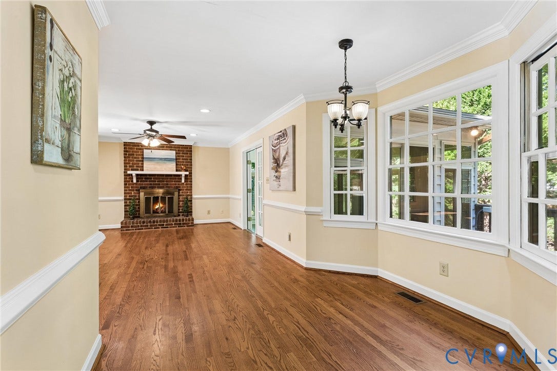 Hardwood-finish flooring, brick fireplace with a white mantel, bay windows with white trim, a chandelier, and crown molding