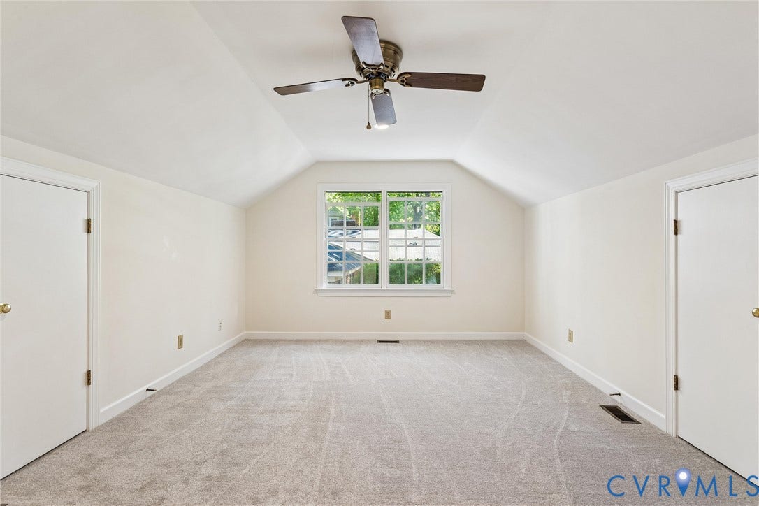 Vaulted ceiling, ceiling fan, central window, light-colored carpeting, two panel doors
