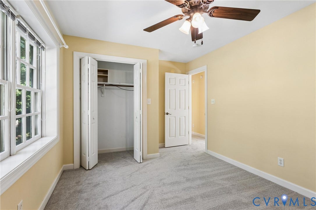 Carpeted room featuring a ceiling fan with light fixture, large multi-pane window, and bifold closet doors