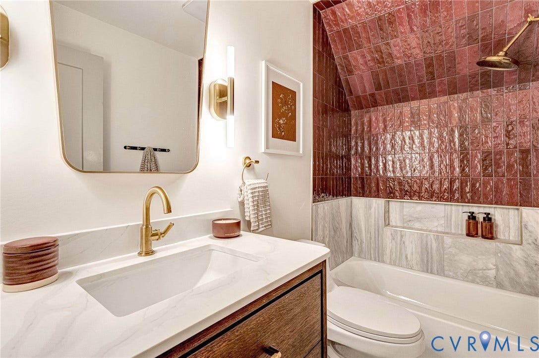 404 Waveny Road, Westham, Henrico, VA 23229 Bathroom featuring a wood-finish vanity with a quartz countertop, brass-finish hardware, a wall-mounted rectangular mirror, and a shower area with glazed burgundy tile and stone-finish wall tile
