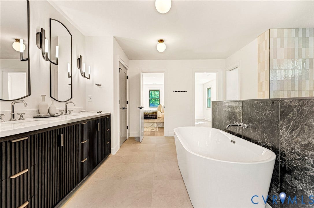404 Waveny Road, Westham, Henrico, VA 23229 Dual-sink vanity with fluted cabinetry and light-toned countertops, freestanding soaking tub, dark stone surround, wall-mounted faucet, and arched-frame mirrors