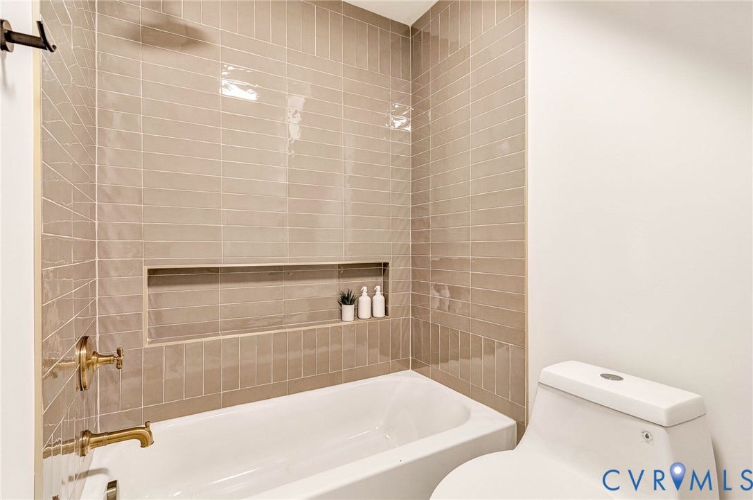 404 Waveny Road, Westham, Henrico, VA 23229 Bathtub surround featuring vertically stacked, glossy taupe subway tiles, a recessed wall niche, and brass-finish plumbing fixtures