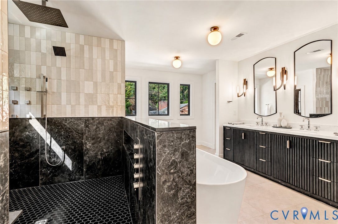 404 Waveny Road, Westham, Henrico, VA 23229 Walk-in shower featuring a rain-style showerhead, dark stone tile wall, and mosaic floor tile; deep soaking tub; dual-sink vanity with fluted cabinetry; arched wall mirrors with integrated lighting