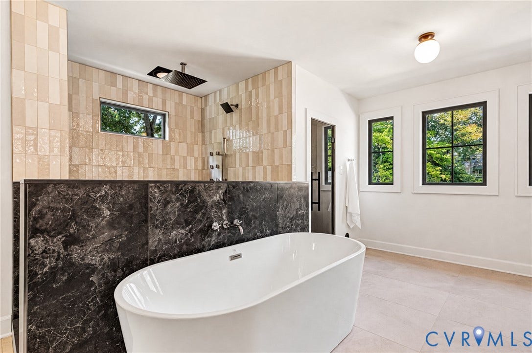 404 Waveny Road, Westham, Henrico, VA 23229 Freestanding soaking tub with wall-mounted plumbing fixtures, dark natural stone half-wall, stacked tile shower surround, and multi-pane windows with dark frames