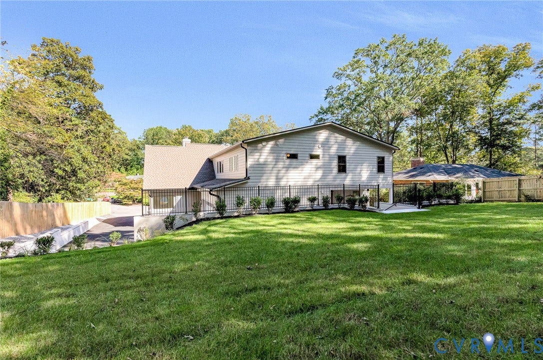 404 Waveny Road, Westham, Henrico, VA 23229 Expansive backyard featuring a manicured lawn, metal perimeter fencing, mature trees, a covered patio structure, and a paved driveway