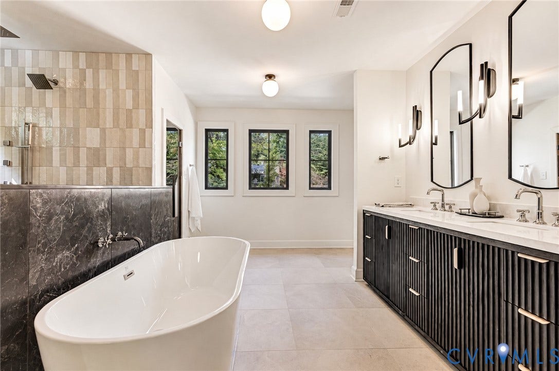 404 Waveny Road, Westham, Henrico, VA 23229 Freestanding soaking tub paired with a stone-accented partition, dual-sink vanity featuring reeded cabinetry, arched wall mirrors, contemporary sconce lighting, and large-format floor tiling