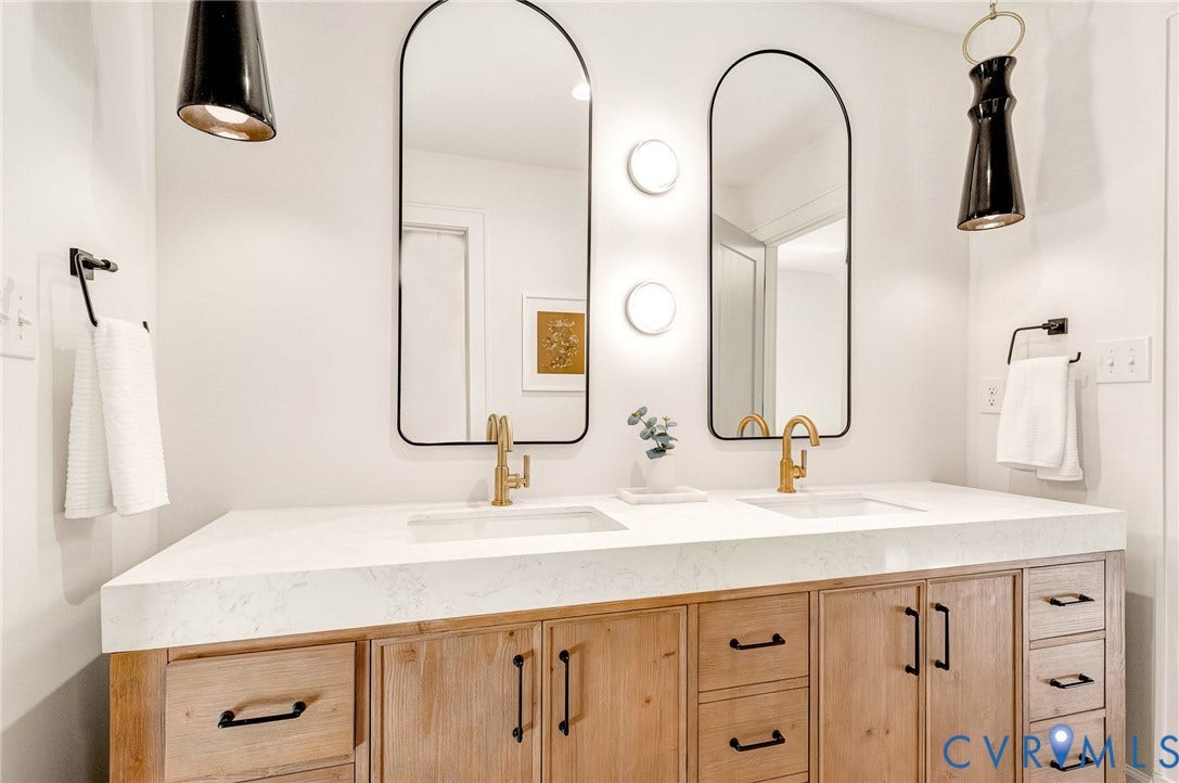 404 Waveny Road, Westham, Henrico, VA 23229 Double vanity featuring a stone-look countertop, integrated dual sinks, natural wood-finish cabinetry, arched mirrors with matte black frames, and brass-tone fixtures