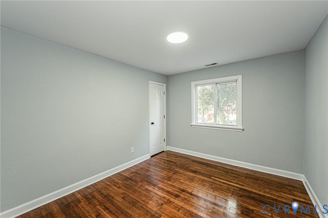 Wood-finish flooring, white trim, single window, flush-mount ceiling light, and a white interior door