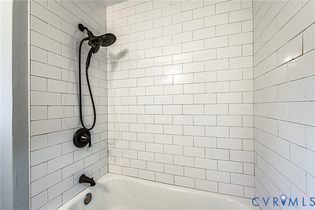White subway tile shower surround with dark grout, matte black shower head, and matching tub spout