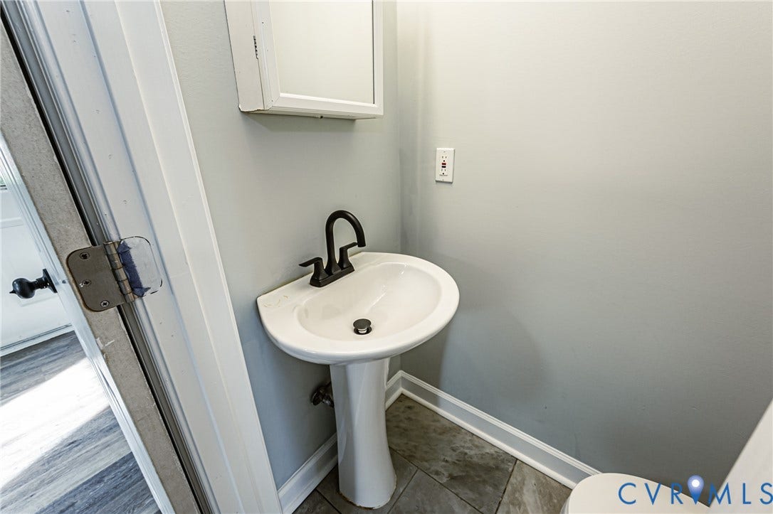 Pedestal sink with a matte black faucet, wall-mounted medicine cabinet, and tiled flooring