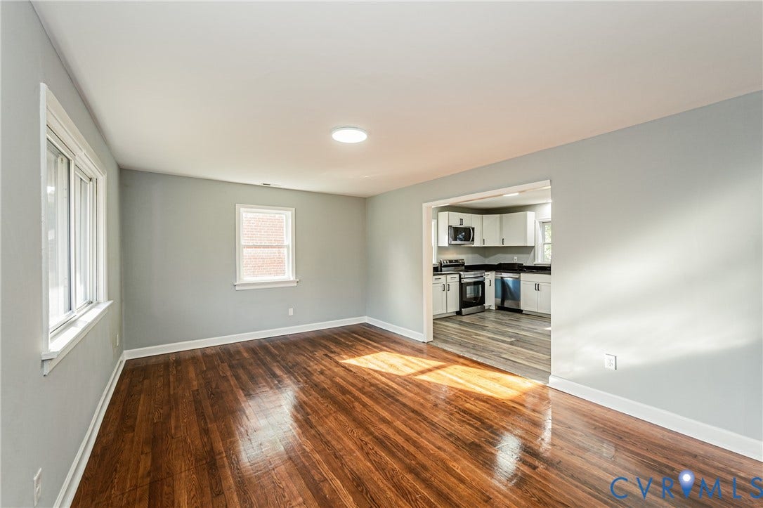 Hardwood flooring, recessed lighting, white trim, light gray walls, kitchen visible through doorway with white cabinetry and stainless steel appliances