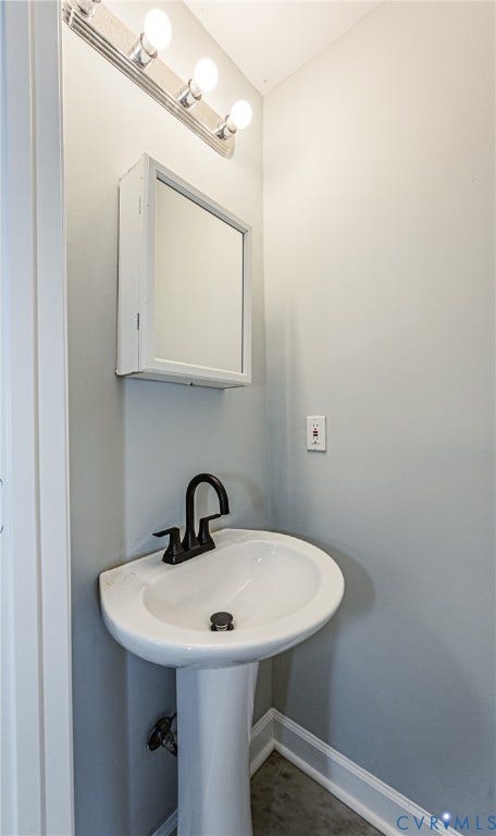 Pedestal sink with a matte black faucet, wall-mounted medicine cabinet, and three-bulb vanity light fixture