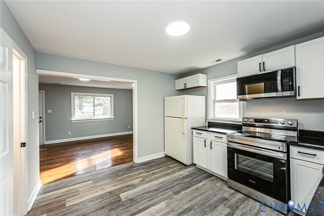 Kitchen featuring white cabinetry, dark countertops, stainless steel range and microwave, and wood-finish flooring