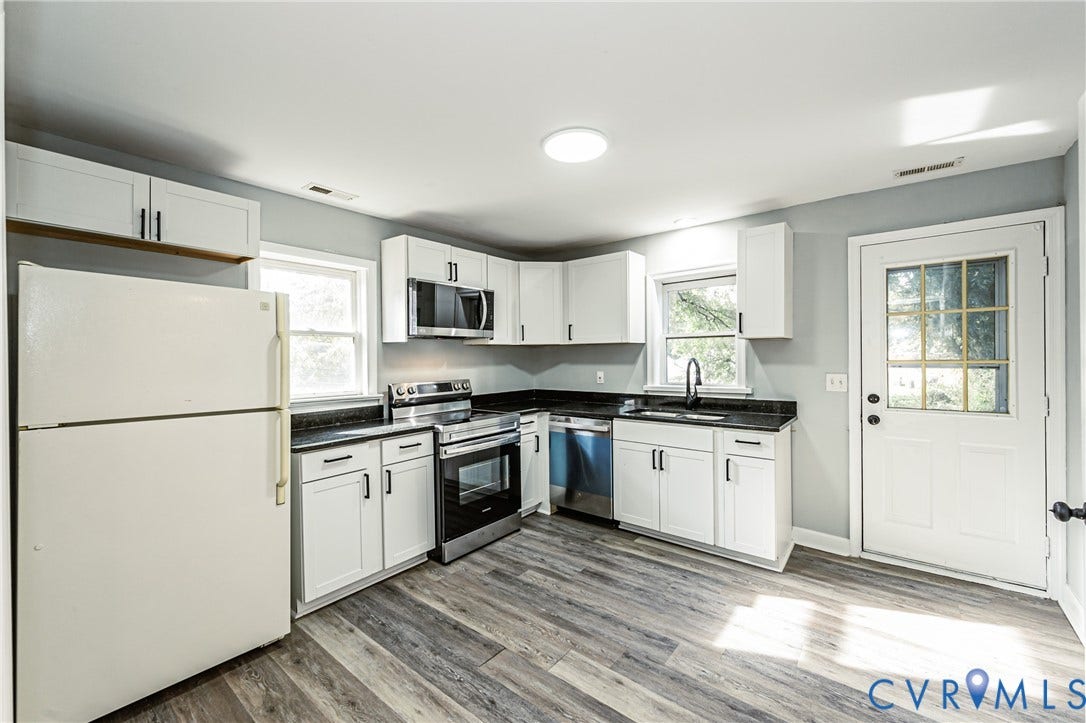 Kitchen featuring white cabinetry, black countertops, stainless steel appliances, and wood-finish flooring