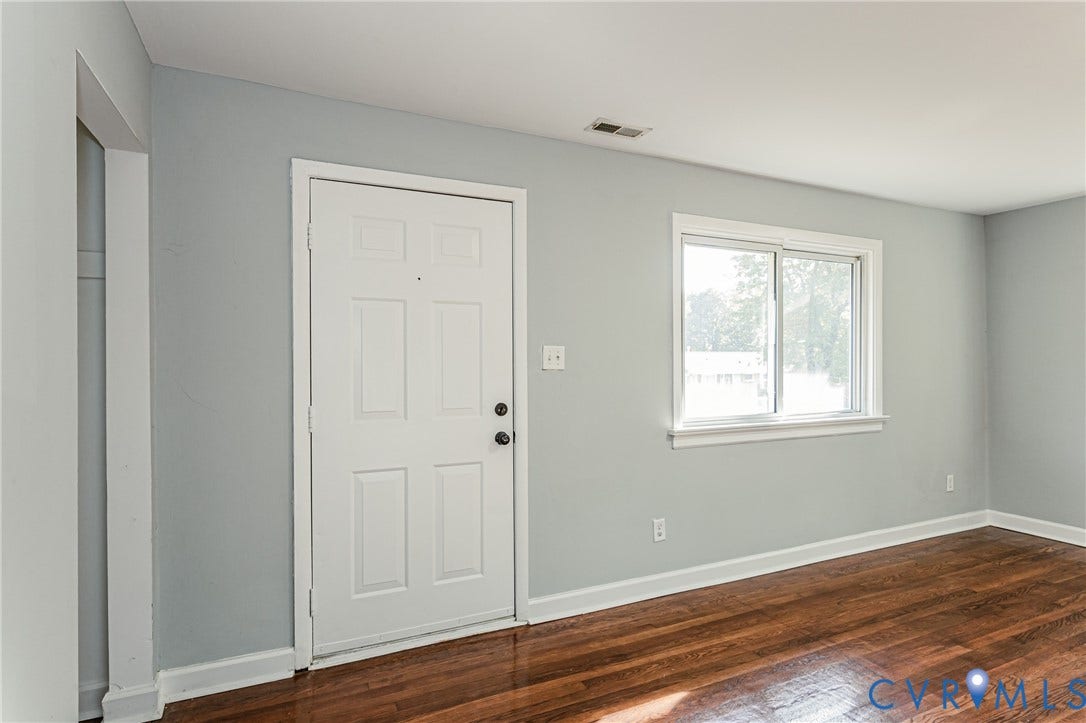 White paneled entry door, wood-finish flooring, and a sliding window with white trim