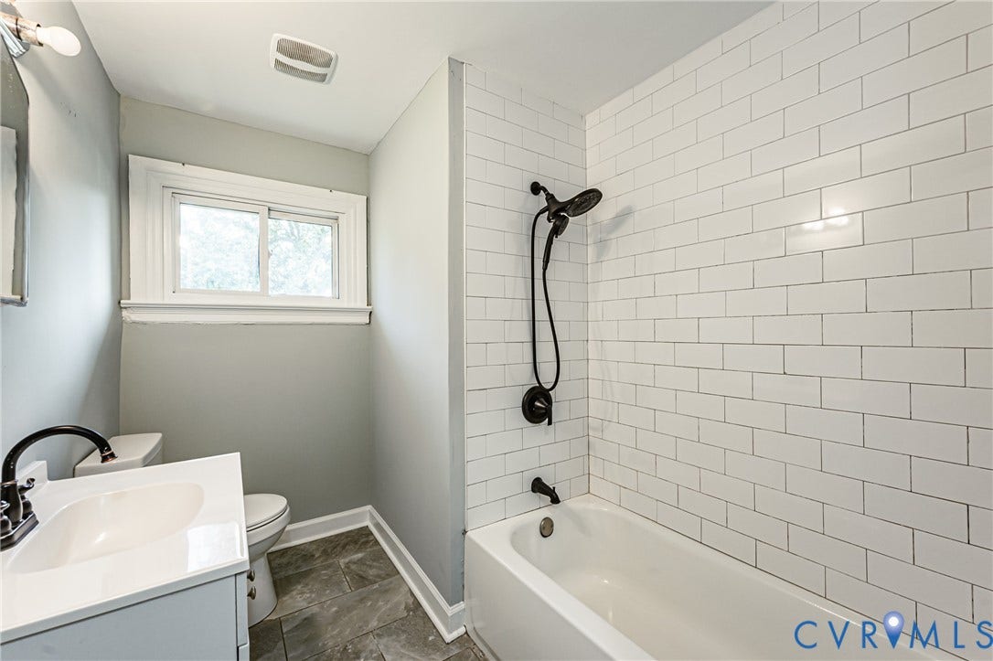 Bathroom featuring a single vanity, dark finish hardware, tiled flooring, bathtub with subway tile surround, and a single window