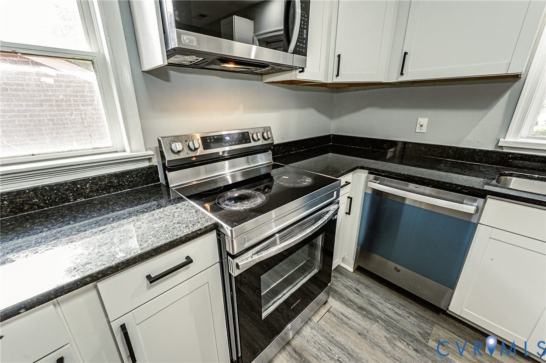 Stainless steel electric range, granite countertops, white cabinetry with black hardware, wood-finish flooring, and a stainless steel dishwasher
