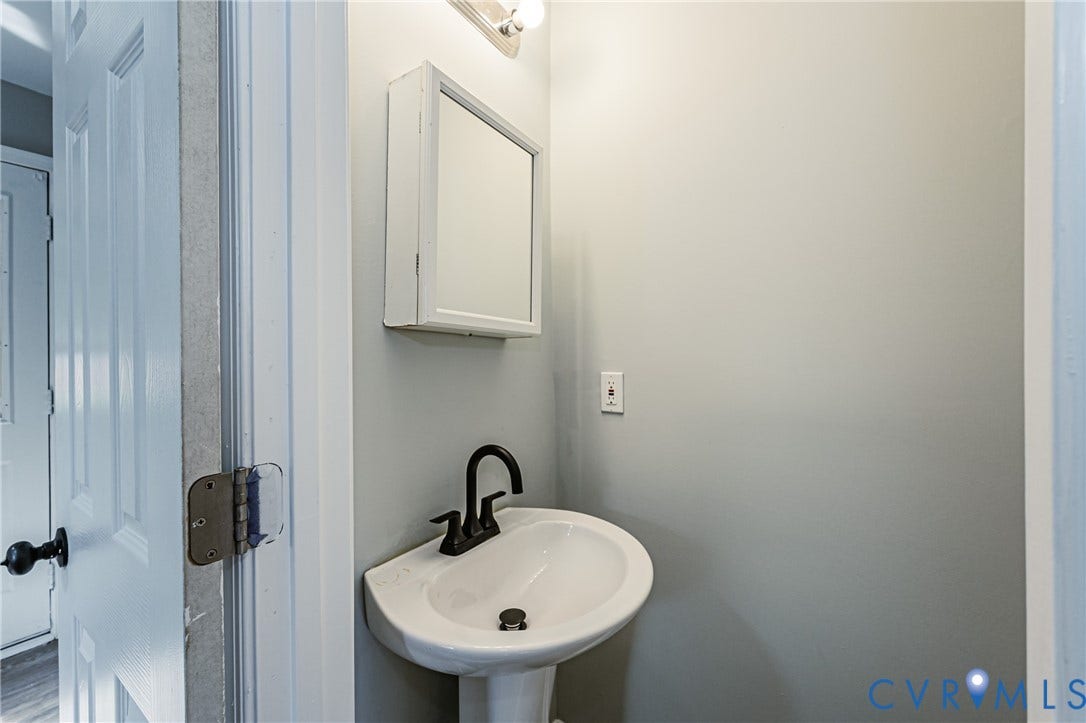 Pedestal sink with black-finish faucet, wall-mounted medicine cabinet with mirror, and overhead lighting fixture