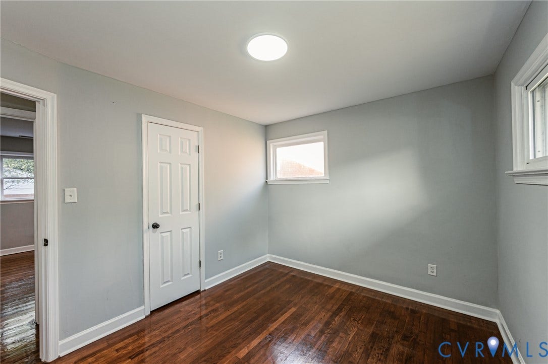 Hardwood flooring, two windows with white trim, a six-panel door, and a circular ceiling light fixture