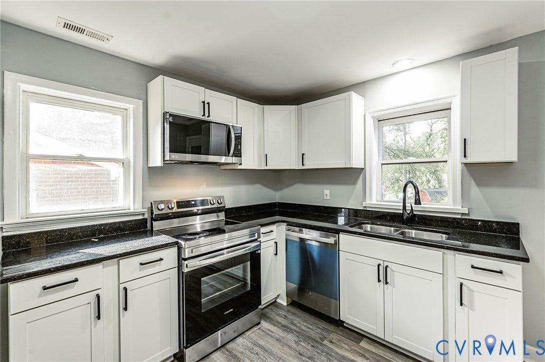 White shaker cabinetry, black countertops, stainless steel appliances, dual basin sink, and wood-finish flooring