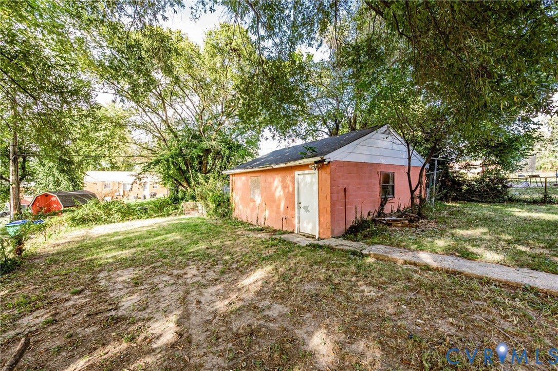 Detached outbuilding with an exterior door and window, situated on a sloped lot with established trees