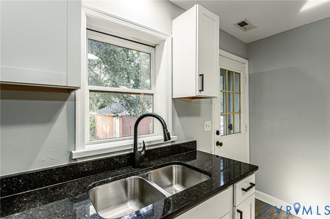 Kitchen featuring a double basin stainless steel sink, black countertop, white cabinetry with black hardware, and wood-finish flooring