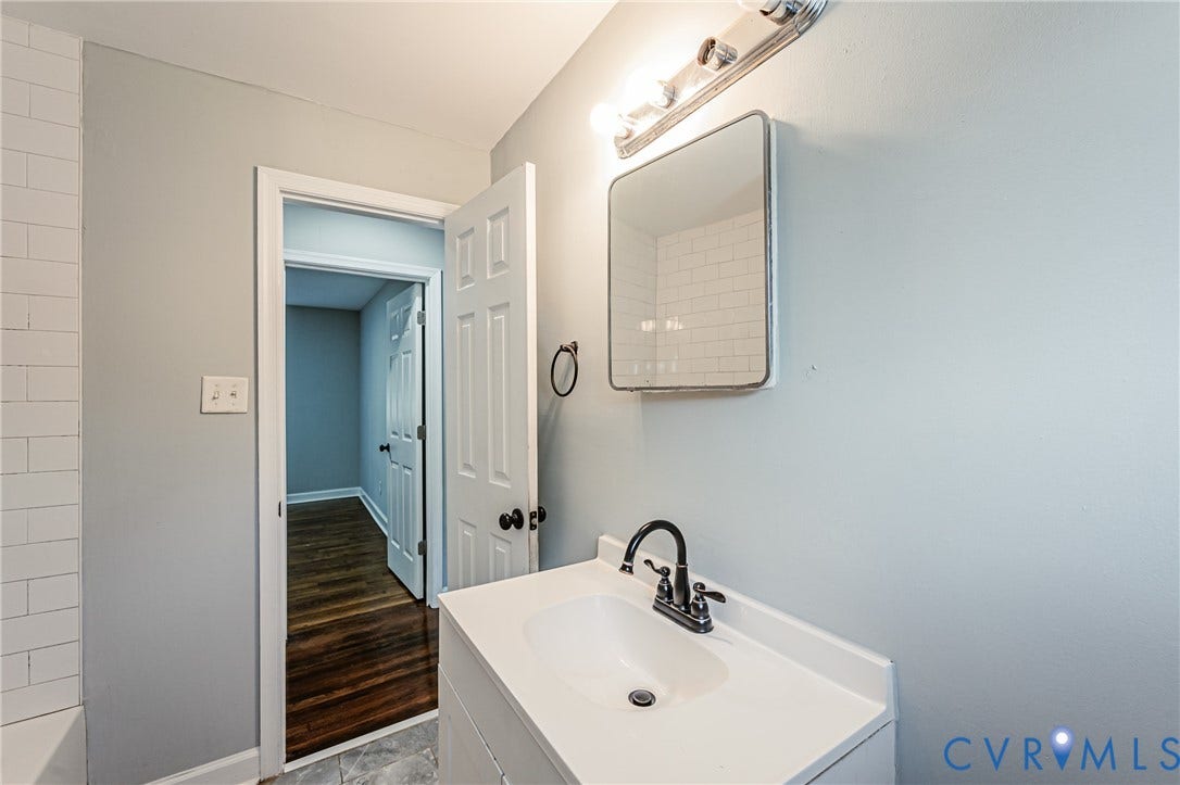 Vanity with integrated sink, oil-rubbed bronze faucet, wall-mounted mirror, and overhead lighting fixture